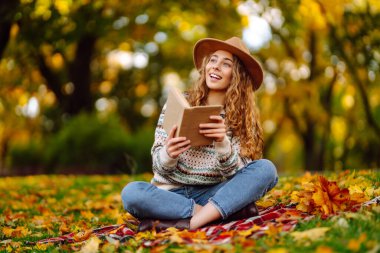 Parkta kitap okuyan bir kadın. Doğanın tadını çıkarma kavramı. Sonbahar havası.