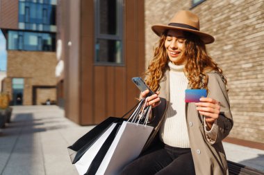 Alışveriş torbaları ve şehirde yürüyen bir kredi kartı tutan genç ve güzel bir kadın. Alışveriş Teklifi. Kara Cuma. Satış, alışverişler, alışveriş, yaşam tarzı konsepti.