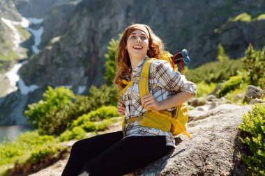 Genç kadın yürüyüşçü kayanın üzerinde duruyor ve dağların manzarasından hoşlanıyor. Aktif yaşam tarzı. Seyahat, macera.