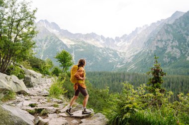 Sırt çantalı, doğa yürüyüşünde gülümseyen bir kadın. Dağ yolunda durup gülümseyen kameraya bakan güzel bir kadın yürüyüşçü. Yaşam tarzı, macera, doğa, aktif yaşam.