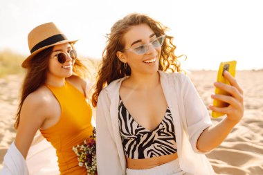 İki güzel arkadaş sahilde selfie çeken kadınlar, açık ve parlak yaz renkleri. Arkadaşlar birlikte. Seyahat, blog, hafta sonu, rahatlama ve yaşam tarzı konsepti.