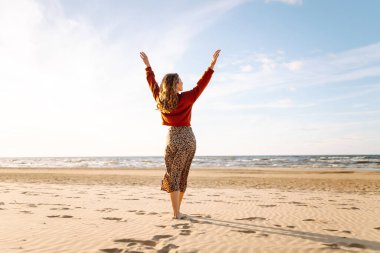 Rüzgarlı bahar gününde kıyıda dinlenen güzel bir kadın. Kaygısız kadın gün batımına bakıyor. Seyahat, yaşam tarzı, macera.