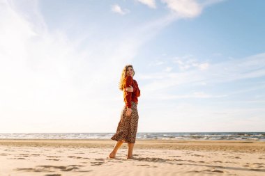 Rüzgarlı bahar gününde kıyıda dinlenen güzel bir kadın. Kaygısız kadın gün batımına bakıyor. Seyahat, yaşam tarzı, macera.