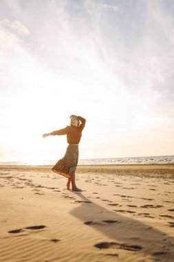 Rüzgarlı bahar gününde kıyıda dinlenen güzel bir kadın. Kaygısız kadın gün batımına bakıyor. Seyahat, yaşam tarzı, macera.