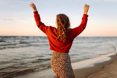 Rüzgarlı bahar gününde kıyıda dinlenen güzel bir kadın. Kaygısız kadın gün batımına bakıyor. Seyahat, yaşam tarzı, macera.