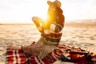 Yalnız romantik bir kadın kumsalda piknikte gün batımını seyrediyor. Seyahat, hafta sonu, rahatlama ve yaşam tarzı konsepti.