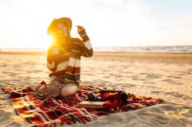 Yalnız romantik bir kadın kumsalda piknikte gün batımını seyrediyor. Seyahat, hafta sonu, rahatlama ve yaşam tarzı konsepti.