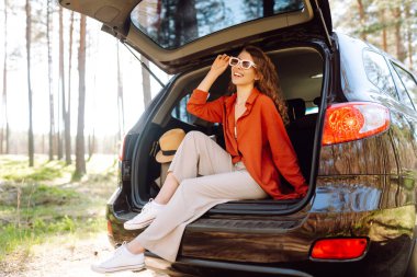 Mutlu kadın doğanın tadını çıkarırken arabasının bagajında tek başına oturuyor. Yaz tatili seyahatleri..