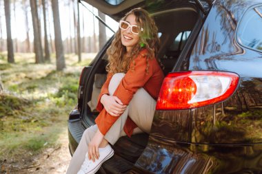 Mutlu kadın doğanın tadını çıkarırken arabasının bagajında tek başına oturuyor. Yaz tatili seyahatleri..