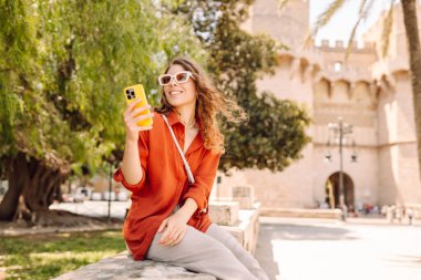 Genç bir kadın şehir merkezinde telefon yürüyüşü yapıyor. Teknoloji, bağlantı, blog yazma, modern yaşam tarzı kavramı.