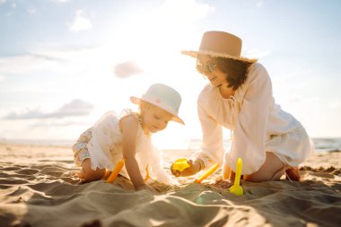 Anne ve kızı kumsalda çocuk oyuncakları ve kumdan kaleyle oynuyorlar. Aile tatili. Güzel sahil sahilinde rahatla..