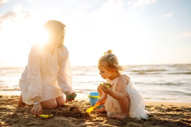 Anne ve kızı kumsalda çocuk oyuncakları ve kumdan kaleyle oynuyorlar. Aile tatili. Güzel sahil sahilinde rahatla..