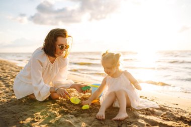 Anne ve kızı kumsalda çocuk oyuncakları ve kumdan kaleyle oynuyorlar. Aile tatili. Güzel sahil sahilinde rahatla..