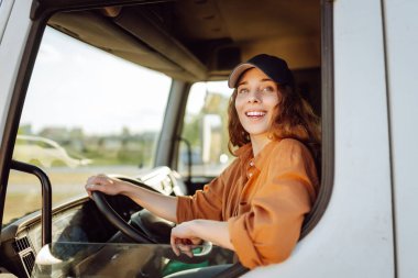 Genç kadın profesyonel kamyon şoförü büyük bir kamyonu ülkenin bir ucundan diğer ucuna sürüyor. Ulaştırma sektörü teması.