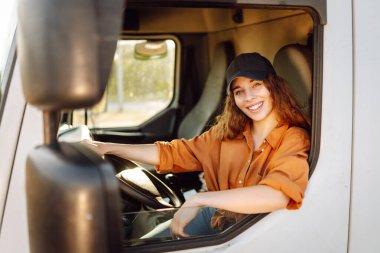 Young woman professional truck driver sitting and driving big truck cross country. Transport industry theme. clipart