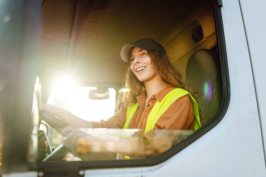 Genç kadın profesyonel kamyon şoförü büyük bir kamyonu ülkenin bir ucundan diğer ucuna sürüyor. Ulaştırma sektörü teması.