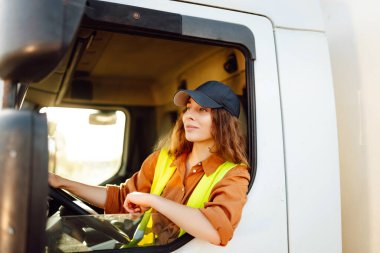 Genç kadın profesyonel kamyon şoförü büyük bir kamyonu ülkenin bir ucundan diğer ucuna sürüyor. Ulaştırma sektörü teması.