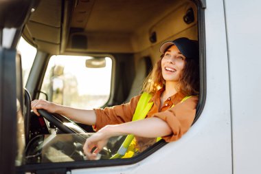 Genç kadın profesyonel kamyon şoförü büyük bir kamyonu ülkenin bir ucundan diğer ucuna sürüyor. Ulaştırma sektörü teması.