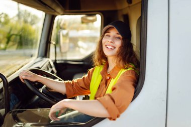 Genç kadın profesyonel kamyon şoförü büyük bir kamyonu ülkenin bir ucundan diğer ucuna sürüyor. Ulaştırma sektörü teması.