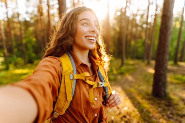 Mutlu kadın turist güneşli bir ormanda yürürken kendi fotoğrafını çekiyor. Güzergahı bul. Seyahat blogu. Macera, tatil.