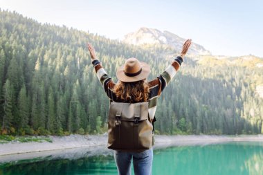 Sırt çantalı kadın gezgin güzel gölün, dağların ve yeşil ormanın tadını çıkarıyor. Çevre turizmi. Etkin yaşam biçimi.
