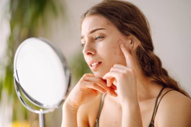 Kadın, sivilce sorununun mini aynayla oluştuğunu görünce yüzü için endişeleniyor. Sivilceler, sivilceler, gözenekler, yaralar. Filtresiz doğal cilt