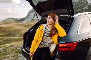 Genç bir kadın bir arabanın bagajında oturuyor. Yolculuk sırasında dur. Arabayla seyahat, turizm, gezi, aktif yaşam tarzı..