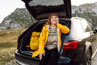 Genç bir kadın bir arabanın bagajında oturuyor. Yolculuk sırasında dur. Arabayla seyahat, turizm, gezi, aktif yaşam tarzı..