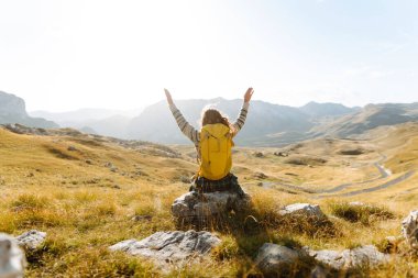 Genç bir kadın kuru otların arasında bir patika boyunca yürüyor. Güneşli bir günde dağlarla kaplı güzel bir manzara. Yürüyüş. Etkin yaşam biçimi