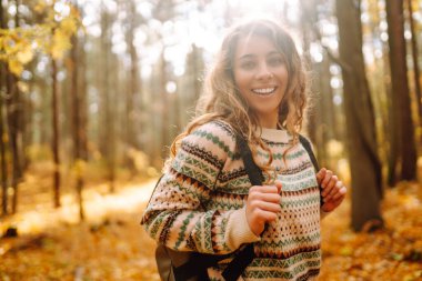 Güneşli bir sonbahar ormanında neşeli bir anın tadını çıkaran bir kadın. Etrafı renkli yapraklar ve yüksek ağaçlarla çevrili.
