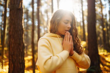 Genç bir kadın, öğleden sonra saatlerinde sakin bir ormanda altın sonbahar yaprakları arasında farkındalık meditasyonu yapar.
