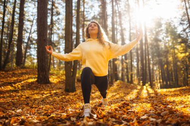 Genç bir kadın, öğleden sonra saatlerinde sakin bir ormanda altın sonbahar yaprakları arasında farkındalık meditasyonu yapar.
