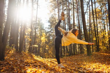 Genç bir kadın, öğleden sonra saatlerinde sakin bir ormanda altın sonbahar yaprakları arasında farkındalık meditasyonu yapar.