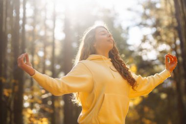 Genç bir kadın, öğleden sonra saatlerinde sakin bir ormanda altın sonbahar yaprakları arasında farkındalık meditasyonu yapar.