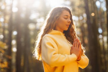 Genç bir kadın, öğleden sonra saatlerinde sakin bir ormanda altın sonbahar yaprakları arasında farkındalık meditasyonu yapar.