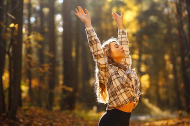 Genç bir kadın, öğleden sonra saatlerinde sakin bir ormanda altın sonbahar yaprakları arasında farkındalık meditasyonu yapar.