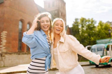 İki arkadaş, tarihi bir şehrin kaldırım taşı sokağında neşeli bir şekilde poz vererek güneşli havalarda dışarıda vakit geçiriyorlar.