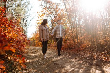 Günbatımında yapraklarla çevrili, sonbahar ormanlarında romantik bir yürüyüş yapan genç bir çift.