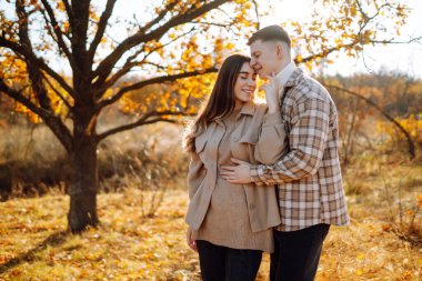 Günbatımında yapraklarla çevrili, sonbahar ormanlarında romantik bir yürüyüş yapan genç bir çift.