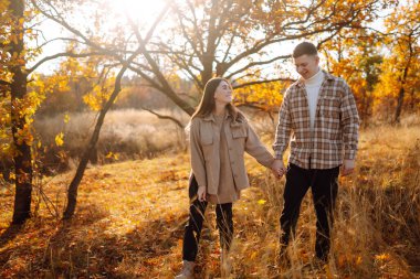 Günbatımında yapraklarla çevrili, sonbahar ormanlarında romantik bir yürüyüş yapan genç bir çift.