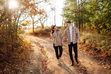 Günbatımında yapraklarla çevrili, sonbahar ormanlarında romantik bir yürüyüş yapan genç bir çift.