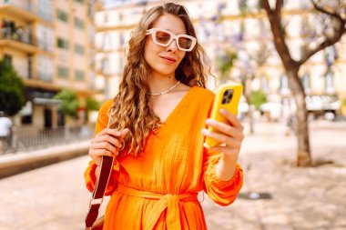 Güneşli bir günün tadını çıkaran bir kadın tarafından giyilen parlak turuncu elbise. Resimli bir şehir ortamında selfie çekerken.