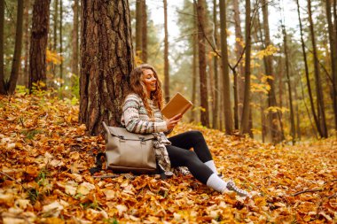 Genç bir kadın renkli yaprakların üzerinde otururken bir kitaba dalmış, sessiz bir anın tadını çıkarıyor. - Evet. Eğitim. Doğadan zevk alma kavramı.