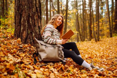 Genç bir kadın renkli yaprakların üzerinde otururken bir kitaba dalmış, sessiz bir anın tadını çıkarıyor. - Evet. Eğitim. Doğadan zevk alma kavramı.