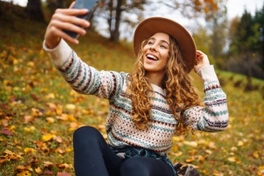 Gülümseyen genç bir kadın, selfie çekerken canlı sonbahar manzarasının tadını çıkarıyor. Seyahat blogu. Macera, tatil konsepti.