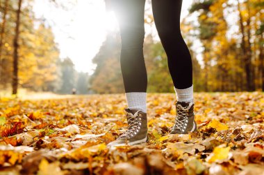 Botları kapatın. Bir insan, canlı sonbahar yapraklarıyla kaplı bir yolda yürüyor, ağaçlarla çevrili, güneşli bir günün tadını çıkarıyor. Boş zamanlardaki sağlıklı yaşam tarzı.