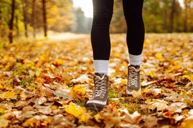Botları kapatın. Bir insan, canlı sonbahar yapraklarıyla kaplı bir yolda yürüyor, ağaçlarla çevrili, güneşli bir günün tadını çıkarıyor. Boş zamanlardaki sağlıklı yaşam tarzı.