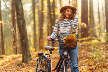 Genç bir kadın renkli yapraklarla dolu bir ormanda bisikletini sürerken güneşli bir sonbahar gününün tadını çıkarıyor. Etkin yaşam biçimi.