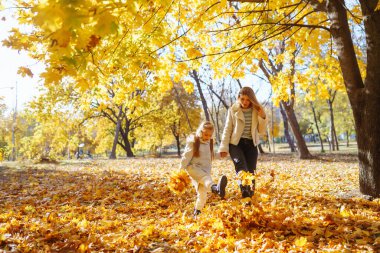 Güzel anne ve kızı, açık bir Ekim günü güneşli bir parkta canlı sonbahar yapraklarında neşeyle oynuyorlar. Aile Günü.