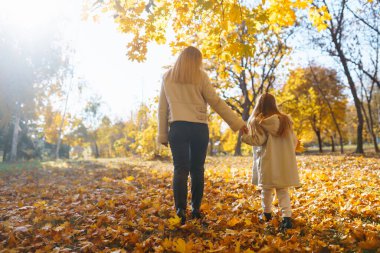Güzel anne ve kızı, açık bir Ekim günü güneşli bir parkta canlı sonbahar yapraklarında neşeyle oynuyorlar. Aile Günü.